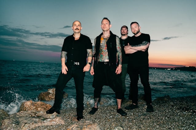 Fotografía promocional de los cuatro integrantes de Trivium junto al mar